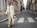 Elegancka kobieta w kremowym płaszczu i spodniach, spacerująca po paryskiej ulicy, uosabia szyk francuskich marek modowych.