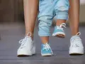 Małe niebieskie buciki na nogach dziecka, idealne na rozmiar buta 3 latka, obok białych sneakersów dorosłego.