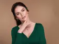 Elegancka kobieta w zielonej sukience prezentuje błyszczące kolczyki i naszyjnik z zielonymi kamieniami. Idealne dodatki do zielonej sukienki.
