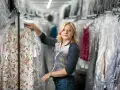 Blondynka w magazynie pralni, tu woman co to za firma? Wieszak z kwiecistą sukienką w folii.