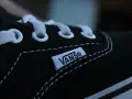 Zbliżenie na czarny but Vans z białymi sznurówkami i charakterystyczną metką. Vans to kultowa firma obuwnicza.