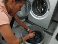 Kobieta w różowej koszulce pierze ciemne ubrania w misce obok pralki. Może to być część rutyny sprzątania w domu w Kilmanock.