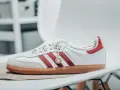 Białe sneakersy Adidas z czerwonymi paskami i zamszowym noskiem. Złoty medalik z logo Adidas i napis "Sporty & Rich" sugerują idealną rozmiarówkę Adidasa.