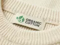 Metka z napisem "ORGANIC COTTON" na kremowym swetrze z prążkowanej dzianiny. To świadczy o tym, że cotton to materiał ekologiczny.