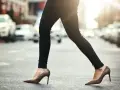 Kobieta w wąskich czarnych spodniach i brązowych szpilkach przechodzi przez ulicę. Idealne buty do wąskich spodni damskich.