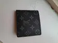 Czarny portfel Louis Vuitton z monogramem na jasnym tle.