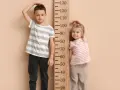 Chłopiec i dziewczynka mierzą wzrost przy drewnianej miarce. Chłopiec ma ok. 110 cm, dziewczynka ok. 90 cm. Jaki rozmiar ubrań pasuje do ich wieku?