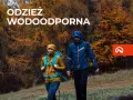 Para idzie przez jesienny las w odzieży wodoodpornej. To oferta firmy Northfinder, która specjalizuje się w odzieży outdoorowej.