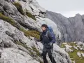 Mężczyzna w kurtce i spodniach trekkingowych z plecakiem wspina się po skalistym zboczu. Idealny przykład, jak się ubrać w góry wiosną.