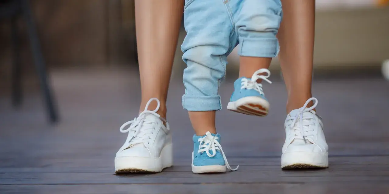 Małe niebieskie buciki na nogach dziecka, idealne na rozmiar buta 3 latka, obok białych sneakersów dorosłego.
