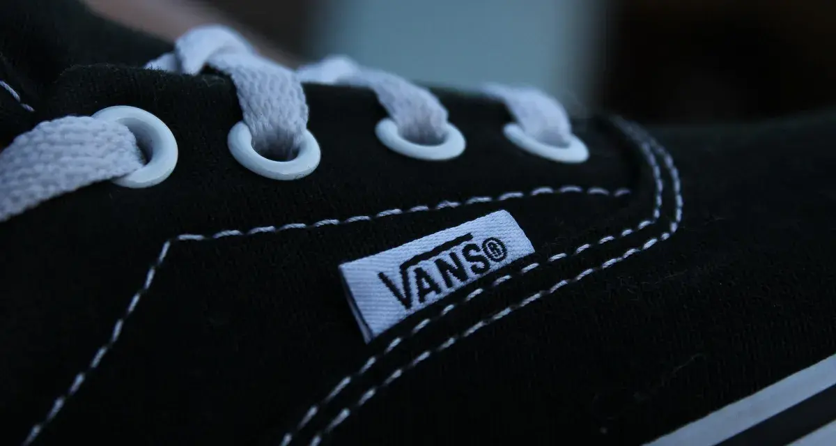 Zbliżenie na czarny but Vans z białymi sznurówkami i charakterystyczną metką. Vans to kultowa firma obuwnicza.