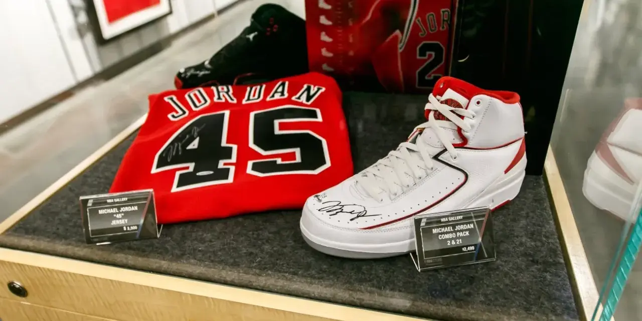 Białe buty sportowe z czerwonymi akcentami, podpisane przez Michaela Jordana, obok koszulki z numerem 45. To pamiątki, które pokazują, jaki michael jordan rozmiar buta nosił.