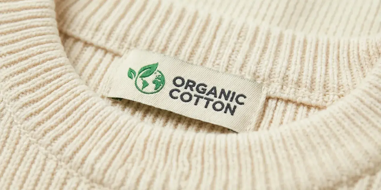 Metka z napisem "ORGANIC COTTON" na kremowym swetrze z prążkowanej dzianiny. To świadczy o tym, że cotton to materiał ekologiczny.