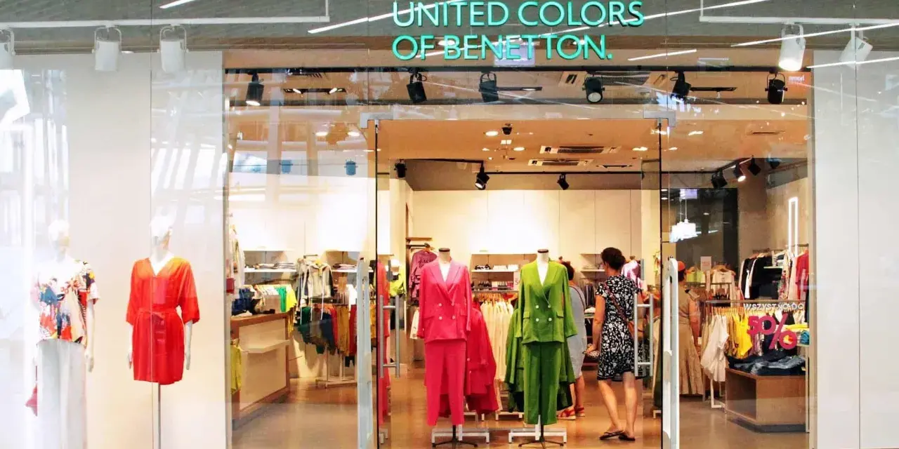 Witryna sklepu United Colors of Bennetton z kolorowymi ubraniami na manekinach i wieszakach.