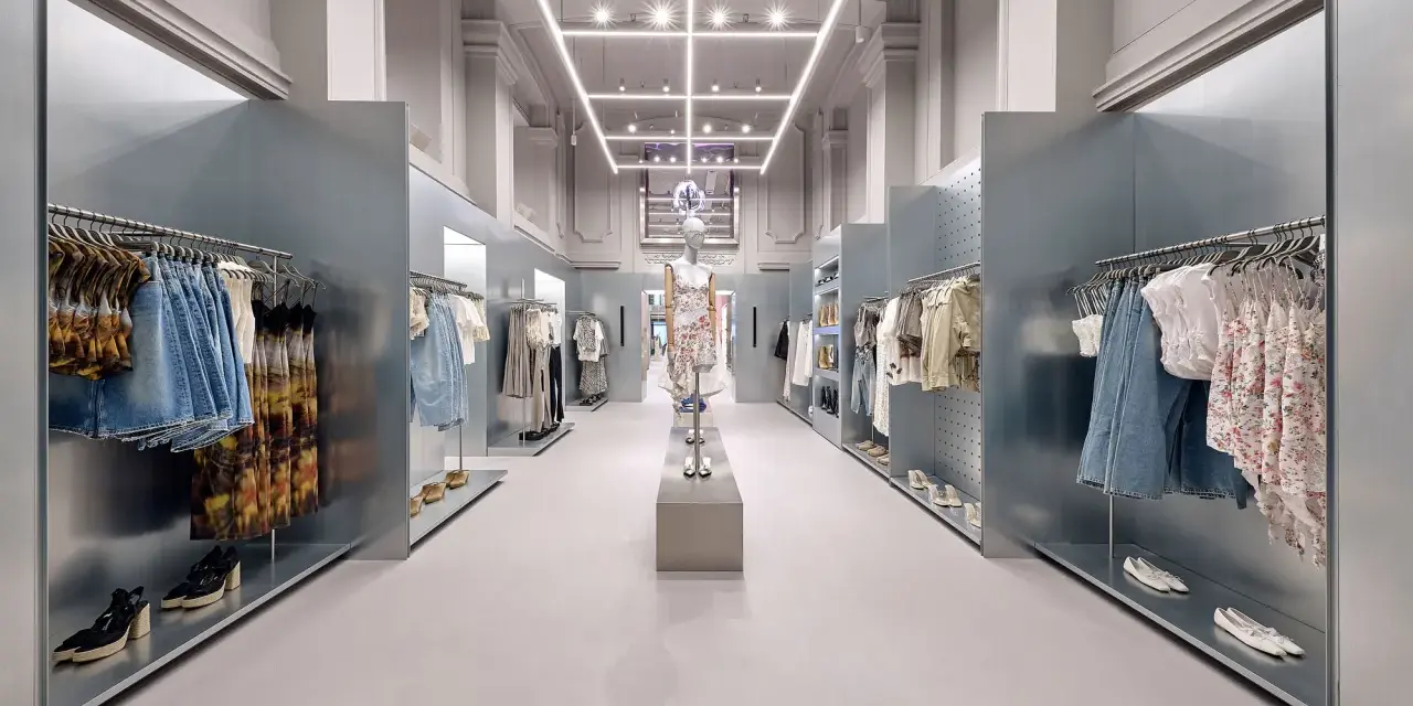 Nowoczesne wnętrze sklepu Bershka z wieszakami pełnymi ubrań i manekinem w centrum.