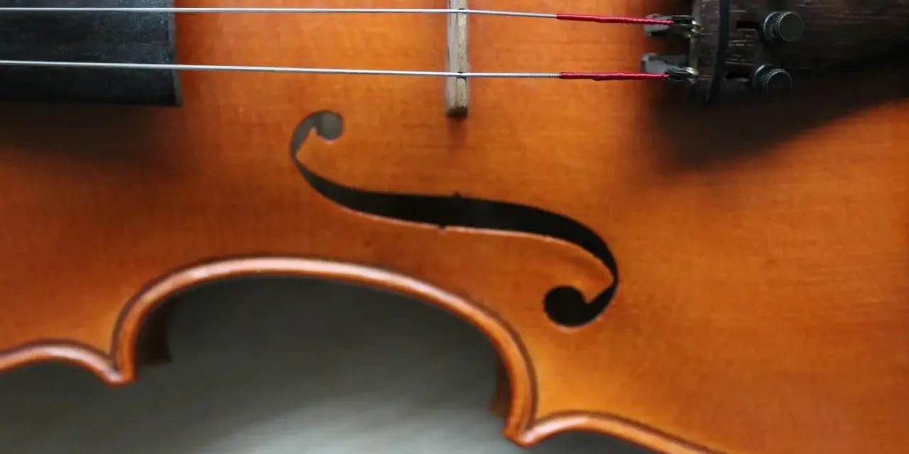 Drewniany korpus skrzypiec, z widocznymi strunami i mostkiem. Ten instrument, być może nawet stradiwarius, emanuje historią i pięknem.