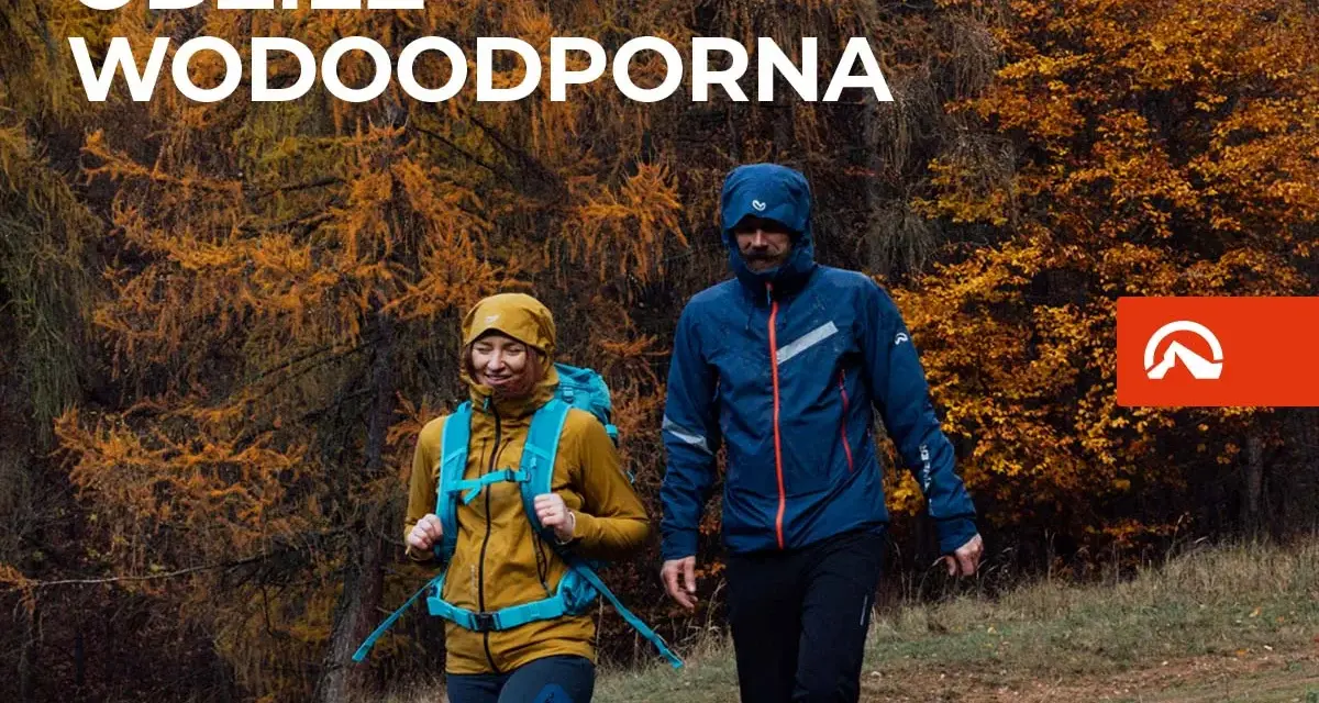 Para idzie przez jesienny las w odzieży wodoodpornej. To oferta firmy Northfinder, która specjalizuje się w odzieży outdoorowej.