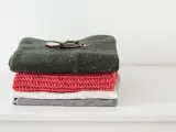 Stosik ubrań: zielony sweter z kropkami, różowy szalik, biała i szara koszulka. Na swetrze leży zegarek, symbol stylu icono couture.