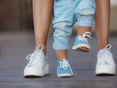 Małe niebieskie buciki na nogach dziecka, idealne na rozmiar buta 3 latka, obok białych sneakersów dorosłego.
