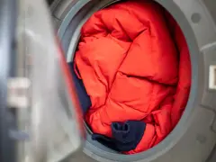Czerwona, puchowa kurtka i granatowy sweter czekają na pranie kurtki zamszowej w pralce.
