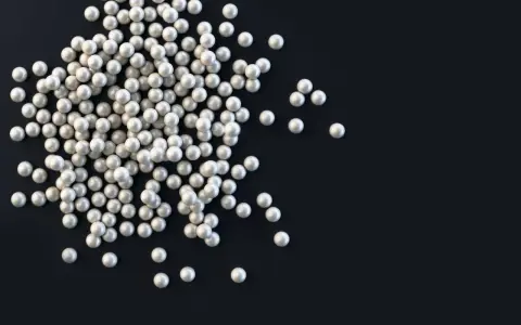 Stos białych pereł, lśniących jak mother of pearl, rozsypany na ciemnym tle.