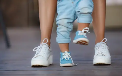 Małe niebieskie buciki na nogach dziecka, idealne na rozmiar buta 3 latka, obok białych sneakersów dorosłego.