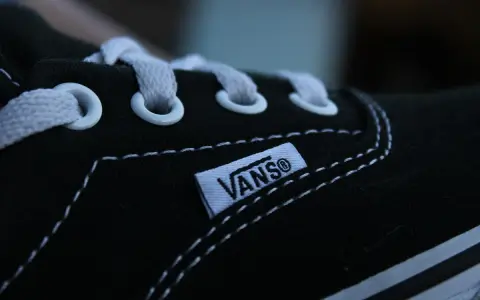 Zbliżenie na czarny but Vans z białymi sznurówkami i charakterystyczną metką. Vans to kultowa firma obuwnicza.