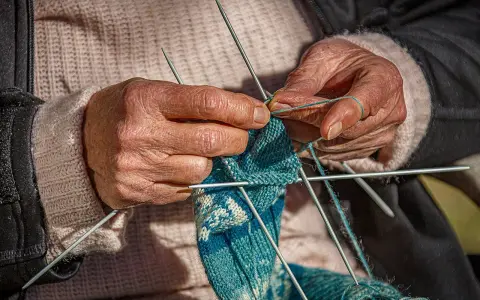 Dłonie tworzą wzorzysty tricot na drutach.