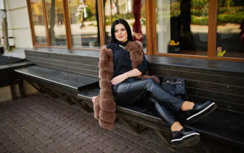 Elegancka kobieta w futrzanej kamizelce i skórzanych spodniach, zastanawia się, jakie buty do skorzanych spodni będą najlepsze. Wybrała czarne, platformowe mokasyny.