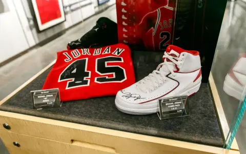 Białe buty sportowe z czerwonymi akcentami, podpisane przez Michaela Jordana, obok koszulki z numerem 45. To pamiątki, które pokazują, jaki michael jordan rozmiar buta nosił.