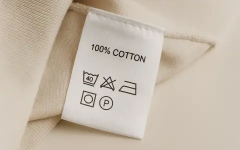 Metka odzieżowa z napisem "100% COTTON" i symbolami pielęgnacji.