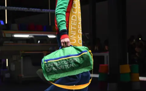 Zielony worek z napisem "UNITED COLORS OF BENETTON" niesiony przez modela w kolorowym swetrze.