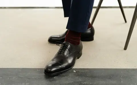 Eleganckie czarne buty męskie, rozmiar buta 50, z bordowymi skarpetkami i granatowymi spodniami.