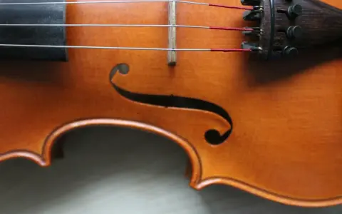 Drewniany korpus skrzypiec, z widocznymi strunami i mostkiem. Ten instrument, być może nawet stradiwarius, emanuje historią i pięknem.