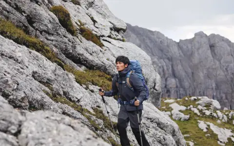 Mężczyzna w kurtce i spodniach trekkingowych z plecakiem wspina się po skalistym zboczu. Idealny przykład, jak się ubrać w góry wiosną.