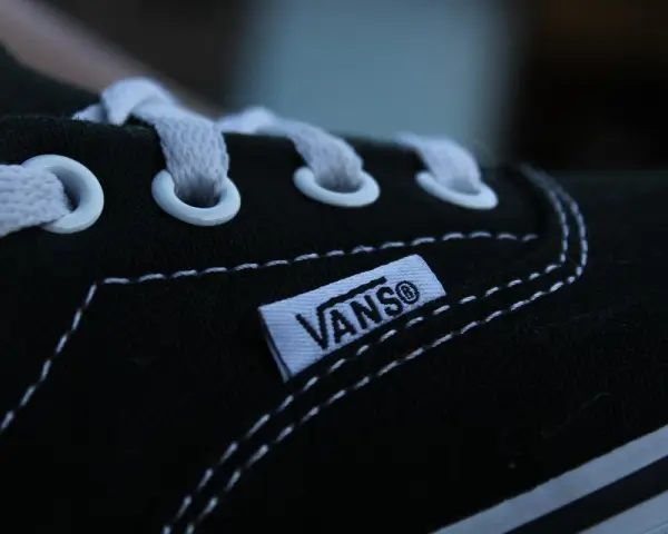Zbliżenie na czarny but Vans z białymi sznurówkami i charakterystyczną metką. Vans to kultowa firma obuwnicza.