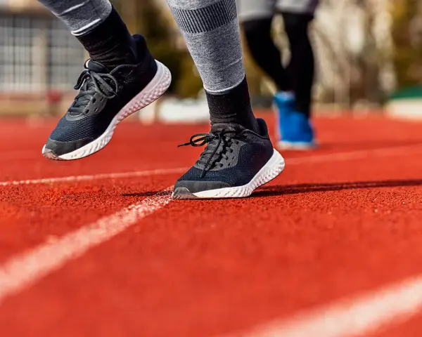 Biegacze na bieżni. Widoczne buty sportowe, podkreślające ruch stopy, czyli supinację i pronację.