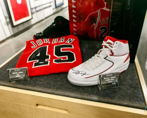 Białe buty sportowe z czerwonymi akcentami, podpisane przez Michaela Jordana, obok koszulki z numerem 45. To pamiątki, które pokazują, jaki michael jordan rozmiar buta nosił.