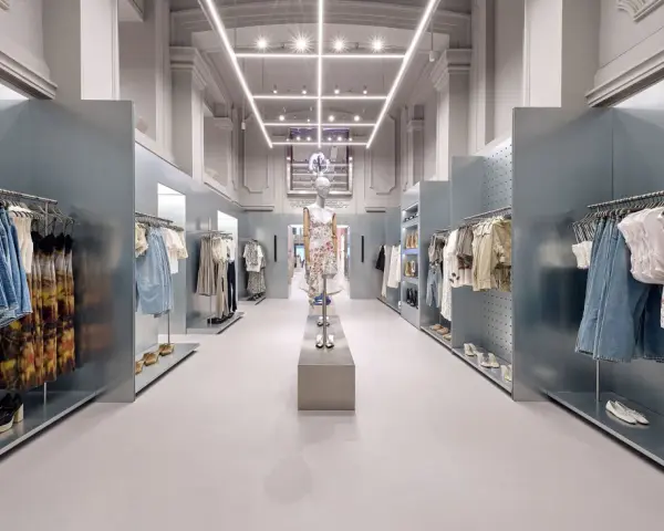 Nowoczesne wnętrze sklepu Bershka z wieszakami pełnymi ubrań i manekinem w centrum.