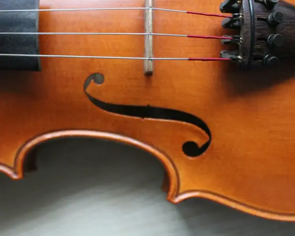 Drewniany korpus skrzypiec, z widocznymi strunami i mostkiem. Ten instrument, być może nawet stradiwarius, emanuje historią i pięknem.