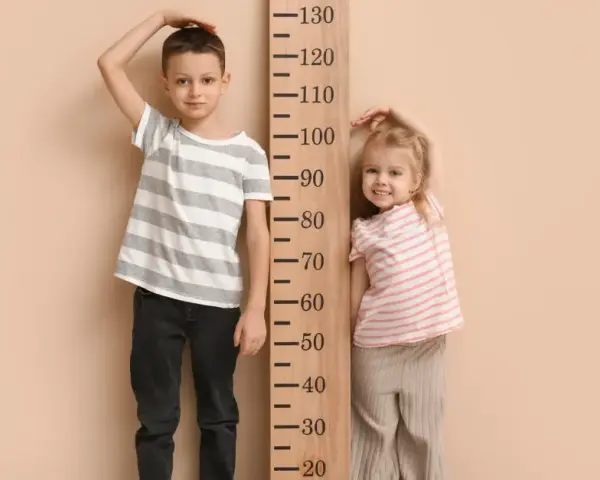 Chłopiec i dziewczynka mierzą wzrost przy drewnianej miarce. Chłopiec ma ok. 110 cm, dziewczynka ok. 90 cm. Jaki rozmiar ubrań pasuje do ich wieku?