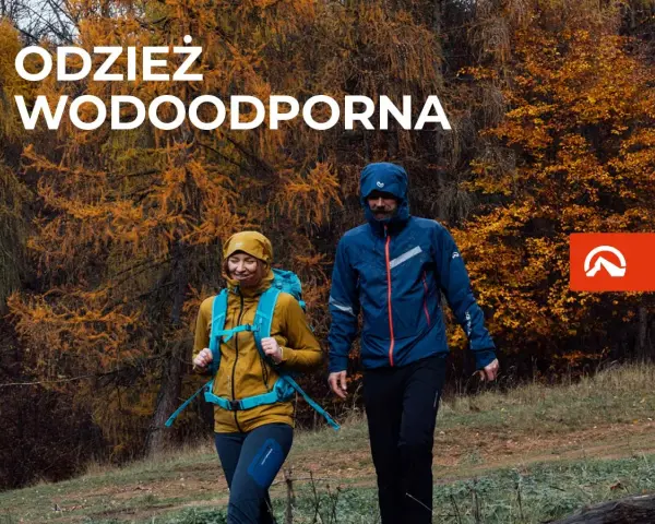 Para idzie przez jesienny las w odzieży wodoodpornej. To oferta firmy Northfinder, która specjalizuje się w odzieży outdoorowej.