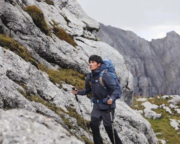 Mężczyzna w kurtce i spodniach trekkingowych z plecakiem wspina się po skalistym zboczu. Idealny przykład, jak się ubrać w góry wiosną.