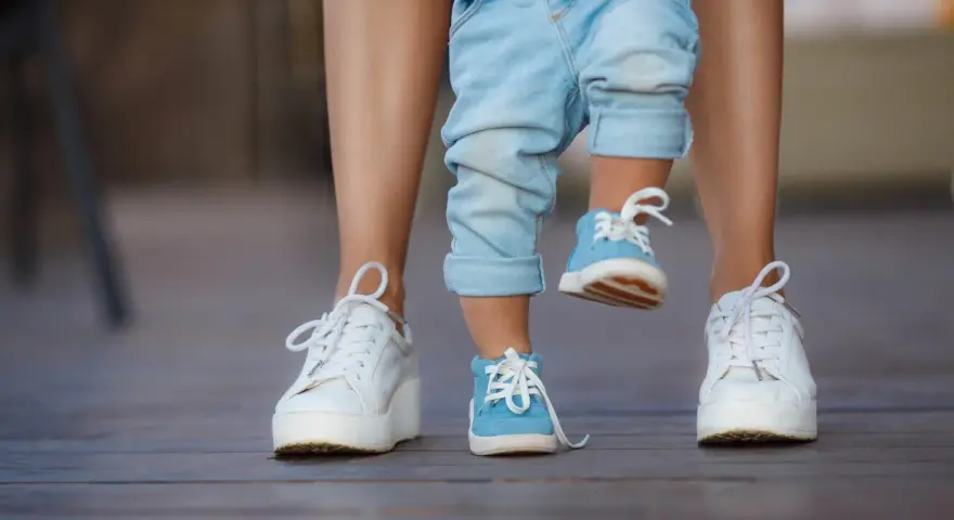 Małe niebieskie buciki na nogach dziecka, idealne na rozmiar buta 3 latka, obok białych sneakersów dorosłego.