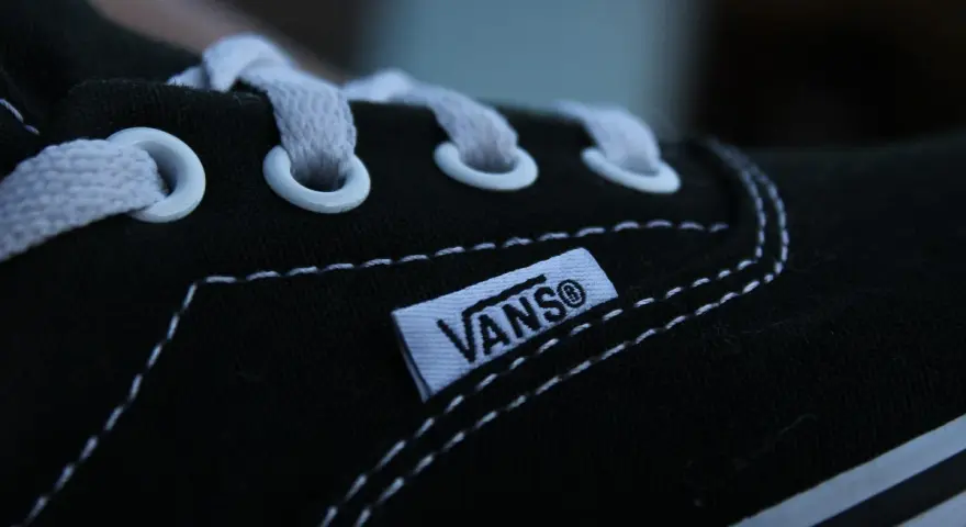 Zbliżenie na czarny but Vans z białymi sznurówkami i charakterystyczną metką. Vans to kultowa firma obuwnicza.