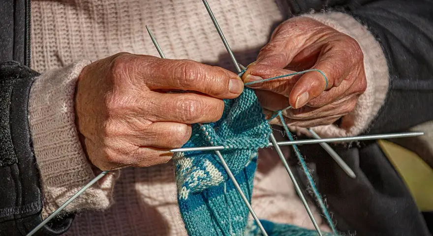 Dłonie tworzą wzorzysty tricot na drutach.