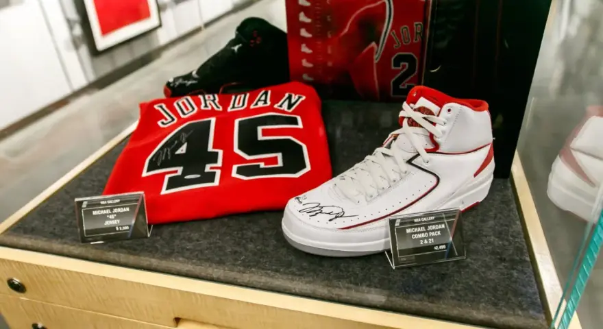 Białe buty sportowe z czerwonymi akcentami, podpisane przez Michaela Jordana, obok koszulki z numerem 45. To pamiątki, które pokazują, jaki michael jordan rozmiar buta nosił.