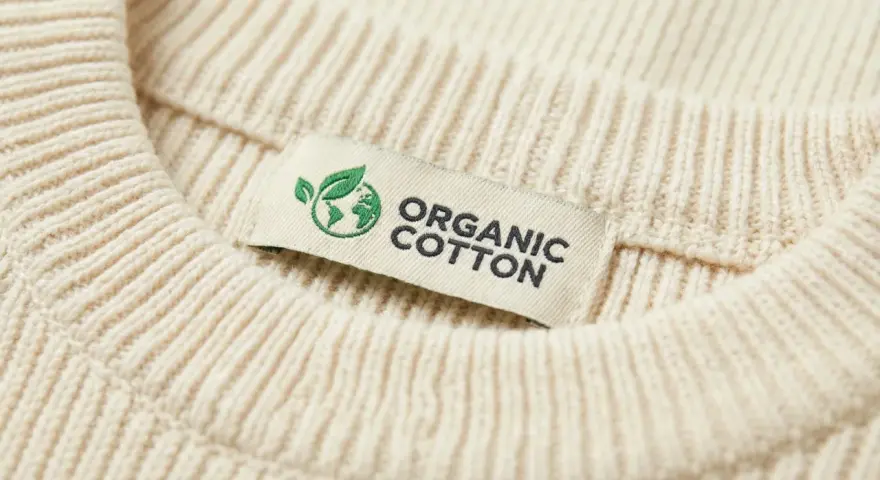 Metka z napisem "ORGANIC COTTON" na kremowym swetrze z prążkowanej dzianiny. To świadczy o tym, że cotton to materiał ekologiczny.
