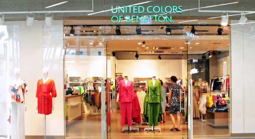 Witryna sklepu United Colors of Bennetton z kolorowymi ubraniami na manekinach i wieszakach.
