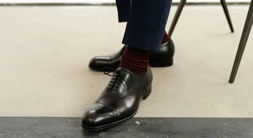 Eleganckie czarne buty męskie, rozmiar buta 50, z bordowymi skarpetkami i granatowymi spodniami.